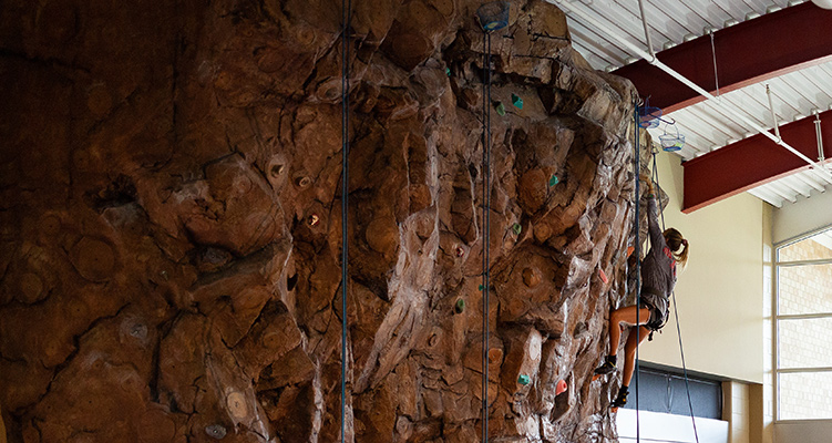 A student climbing the rock wall in the Red WOLF Center