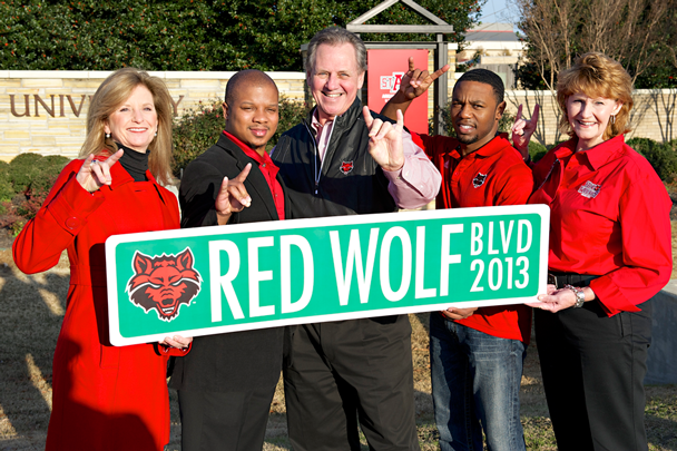 A-State campus leadership holds the Red Wolf Blvd sign in front of Stadium Blvc