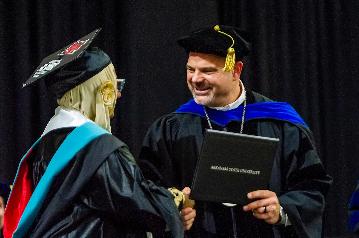 Chancellor Todd Shields shaking a graduate's hand on the commencement stage
