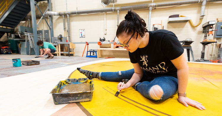 A student painting a set for an upcoming production