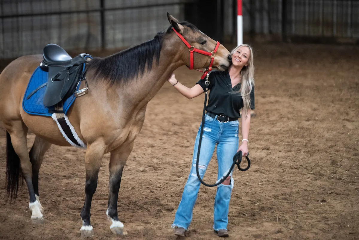 A student poses with a horse in the Equine Center