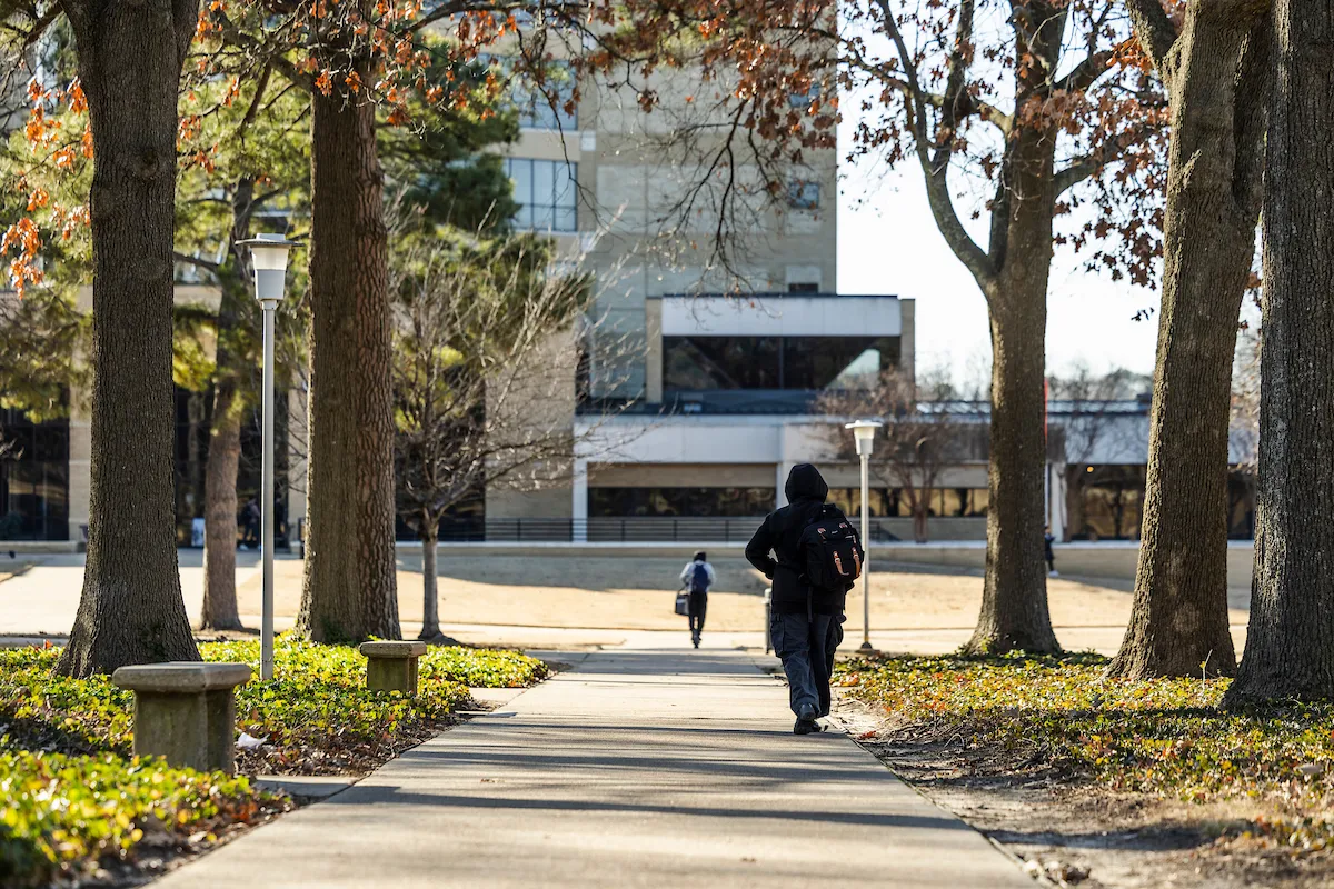 A student walks down a path toward the library on the A-State campus