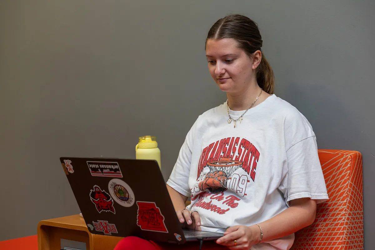 A student in A-State clothes works on a laptop
