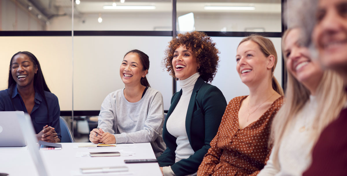 A group of smiling women sitting at a boardroom table.