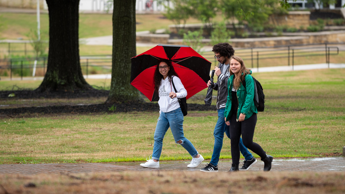 Smiling students walking across campus on a rainy day