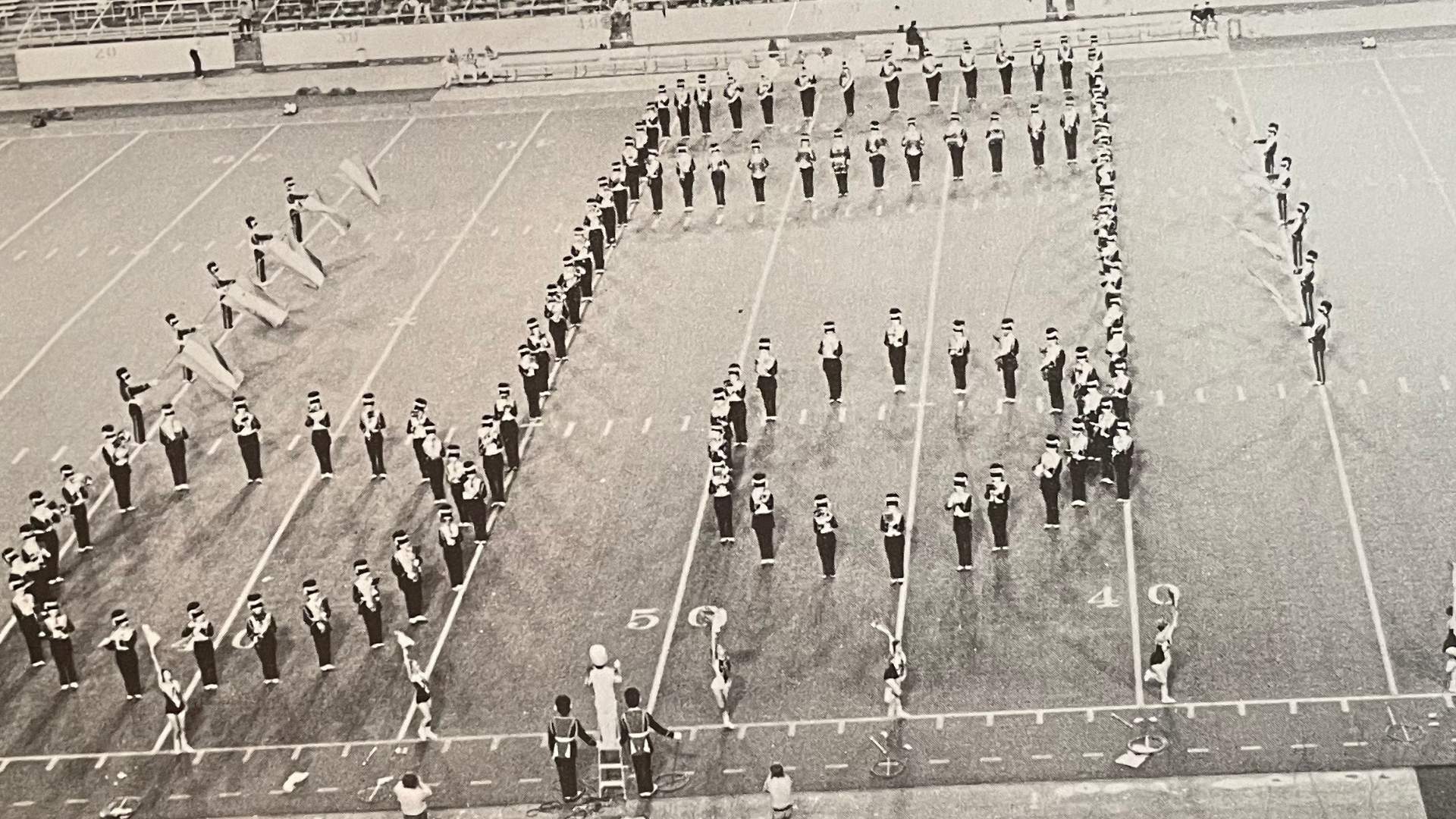 Historical Marching Band photo of the band on the field in a formation that creates two beamed 16th notes.