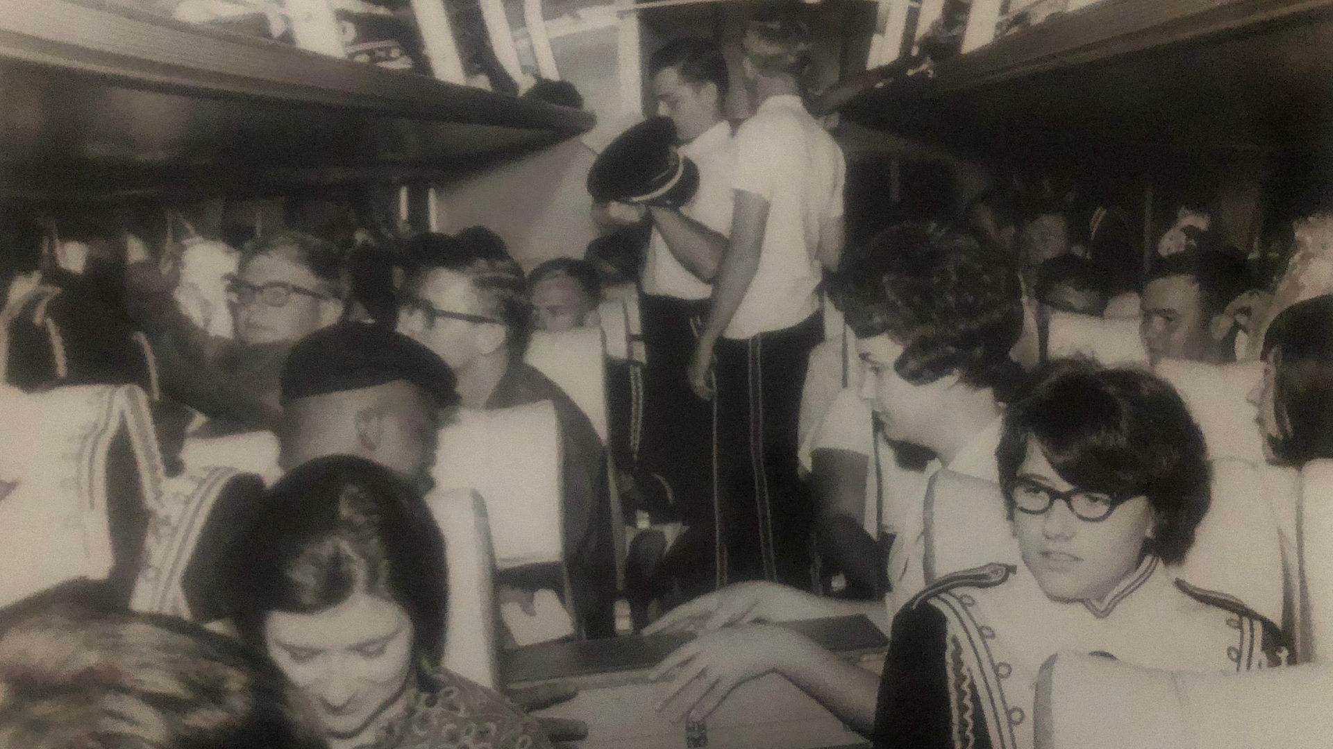 Candid photo of marching band students on a bus with their uniforms on.  The photo is from the mid-1900s.