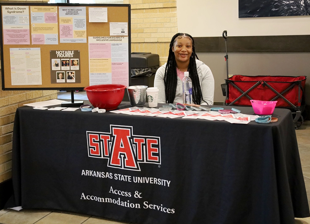 Student at an Access and Accommodations table event with poster about Down Syndrome.