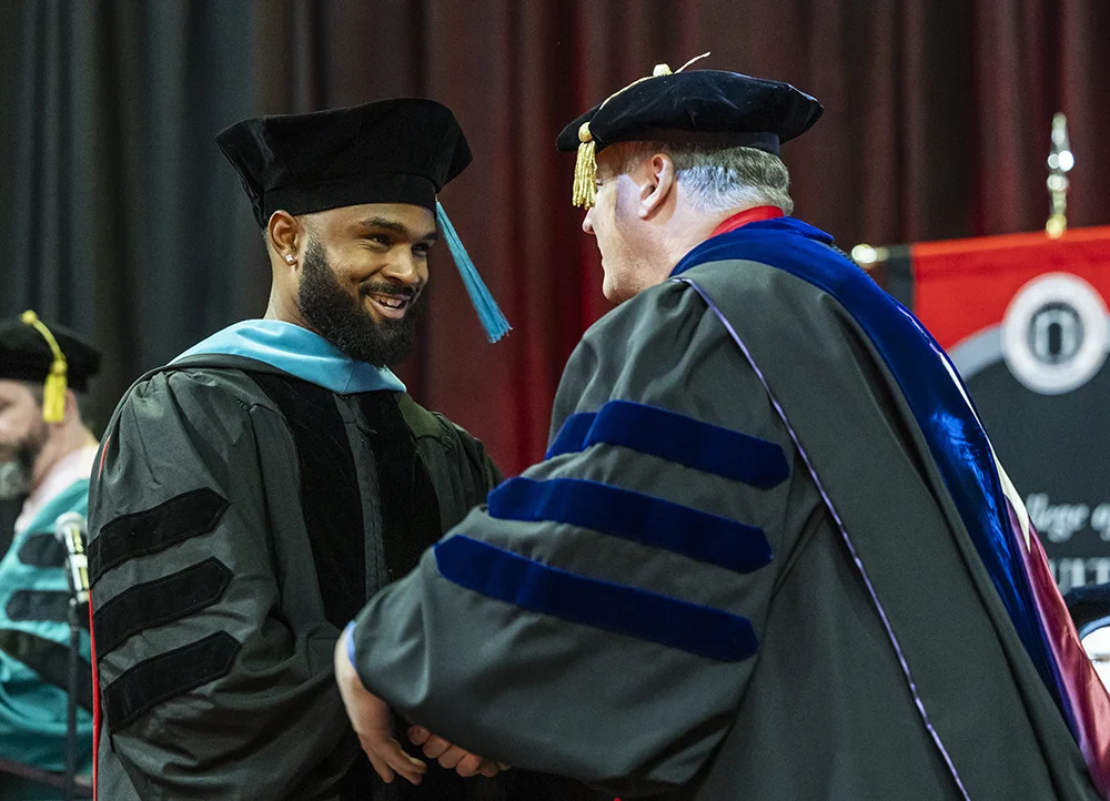 Graduate in doctoral regalia shaking hands at commencement.