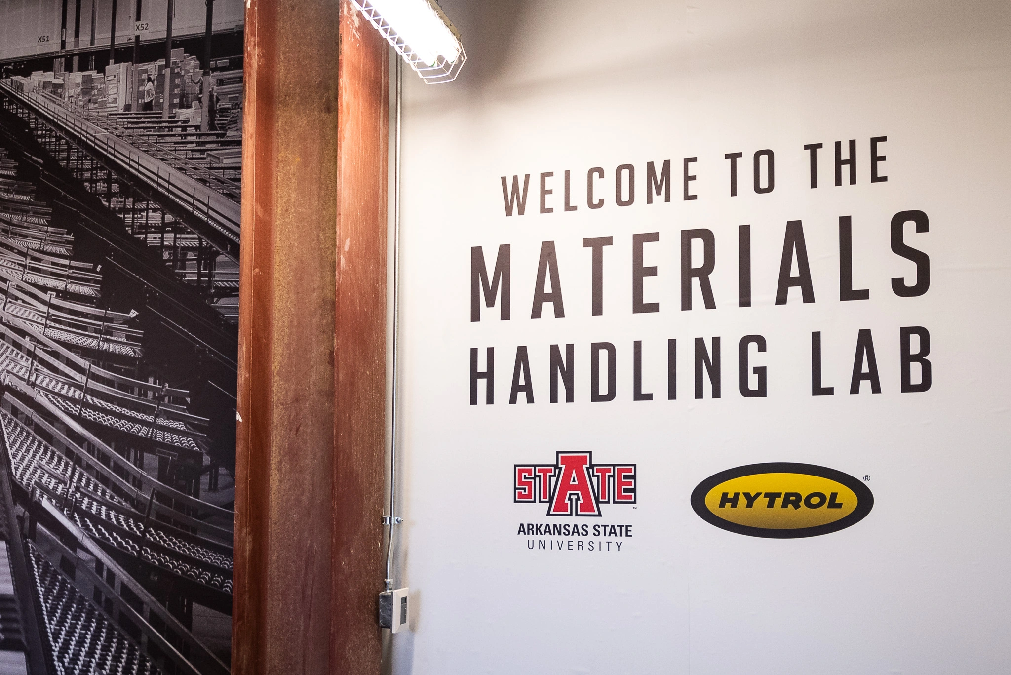Welcome sign for the Arkansas State–Hytrol Materials Handling Lab displayed on an interior wall.