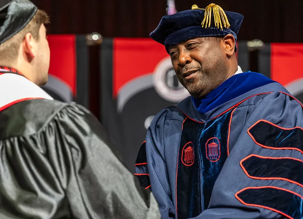 Dr. Calvin White shaking a graduate's hand on the commencement stage