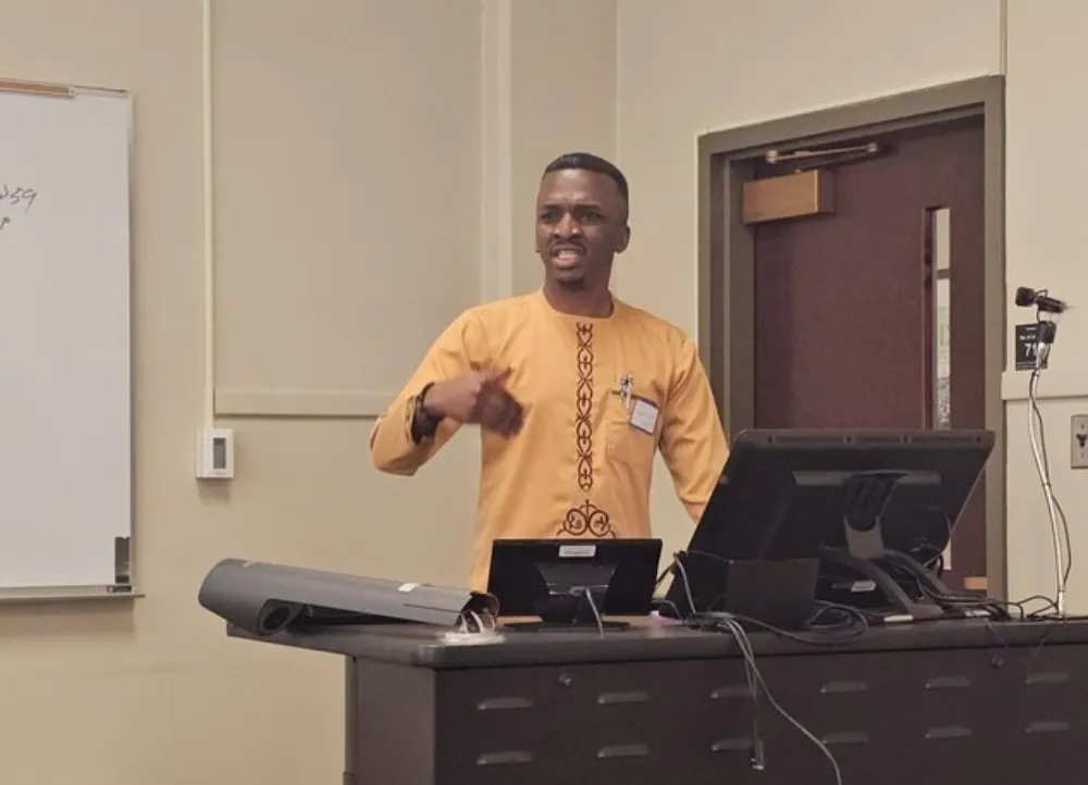 Lucky Ihedigbo presenting his research to others as he stands at a podium.