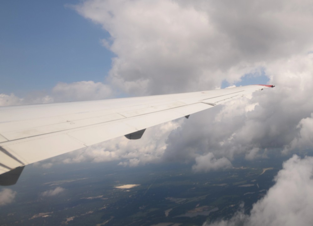 An airplane wing flying in front of a cloudy sky