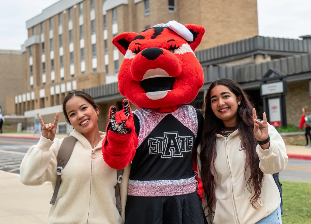 Scarlett with students outside giving a redwolves hand sign.