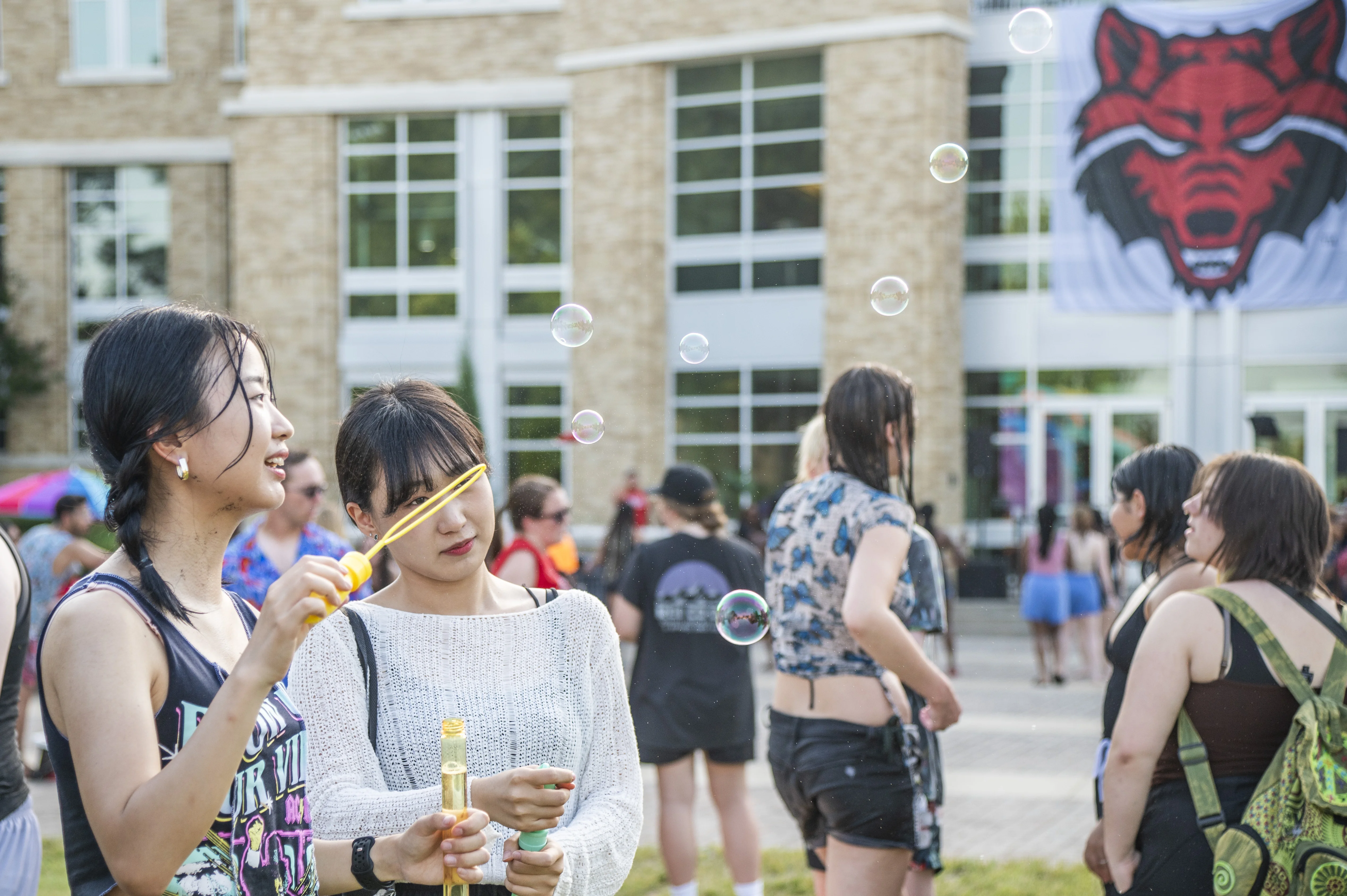 Students at campus event blowing bubbles outside.