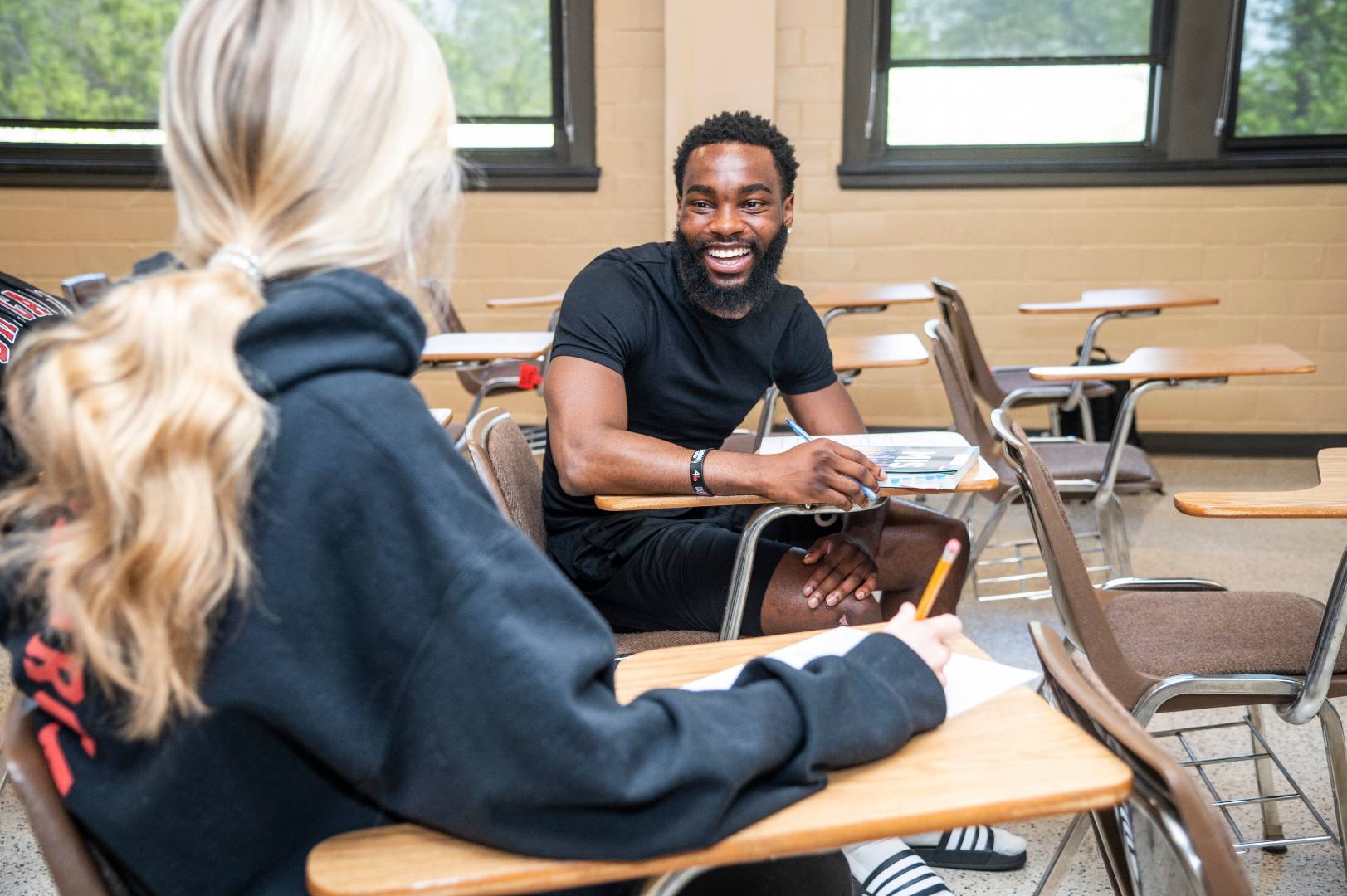 A student sitting at a desk and smiling at someone in the foreground.