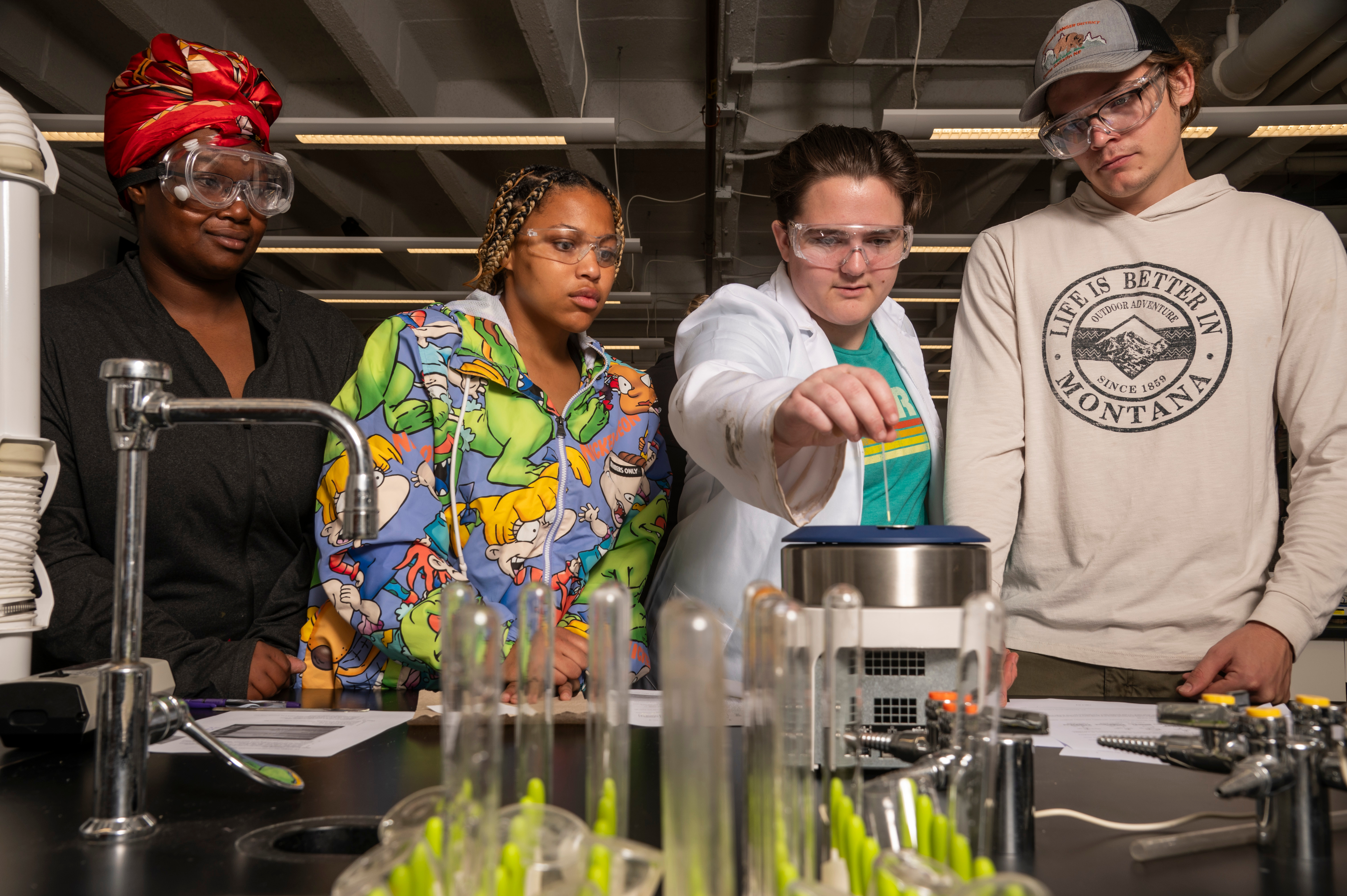 A group of students huddle around a table to watch their professor perform an experiment.