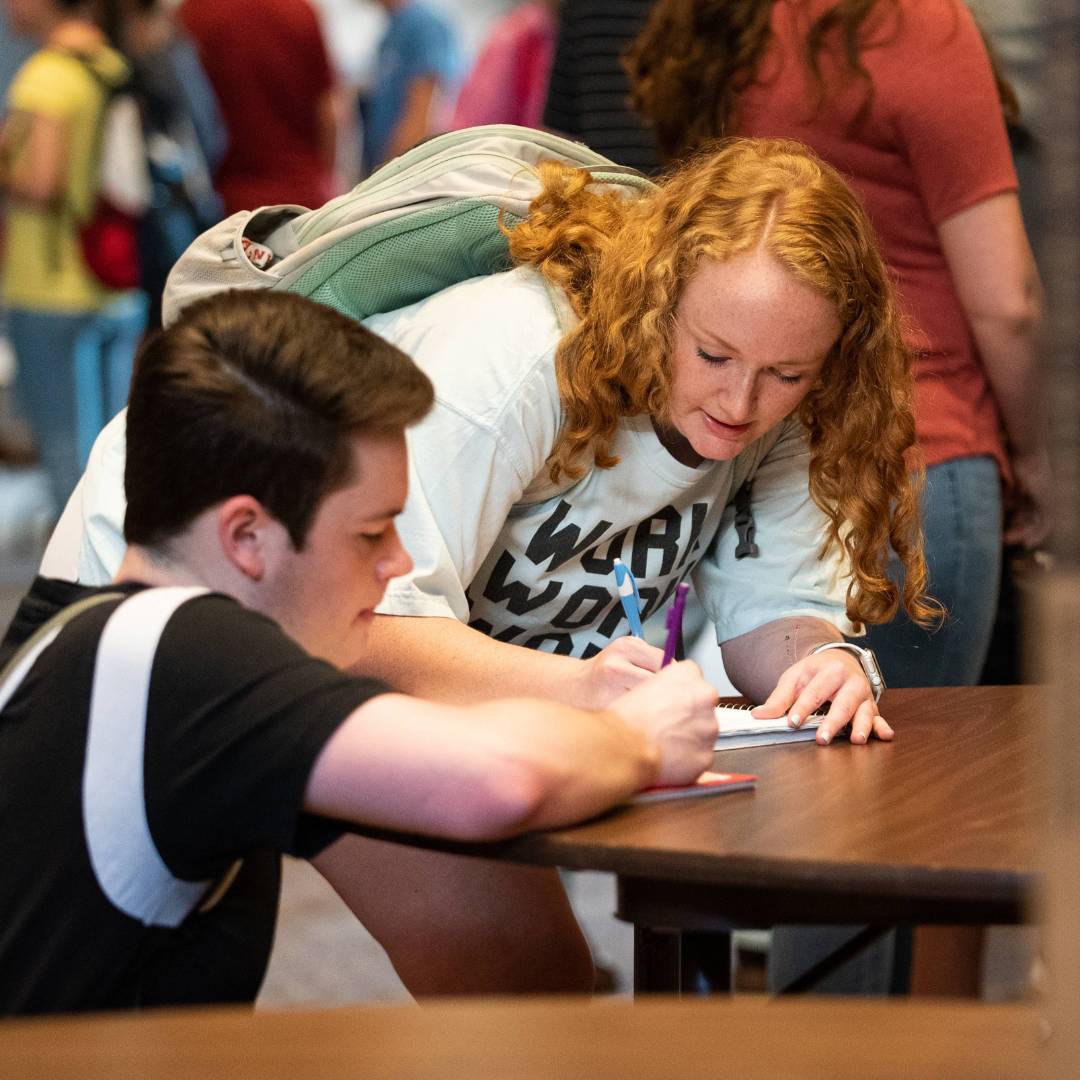 Two students crouching at table and writing on a piece of paper