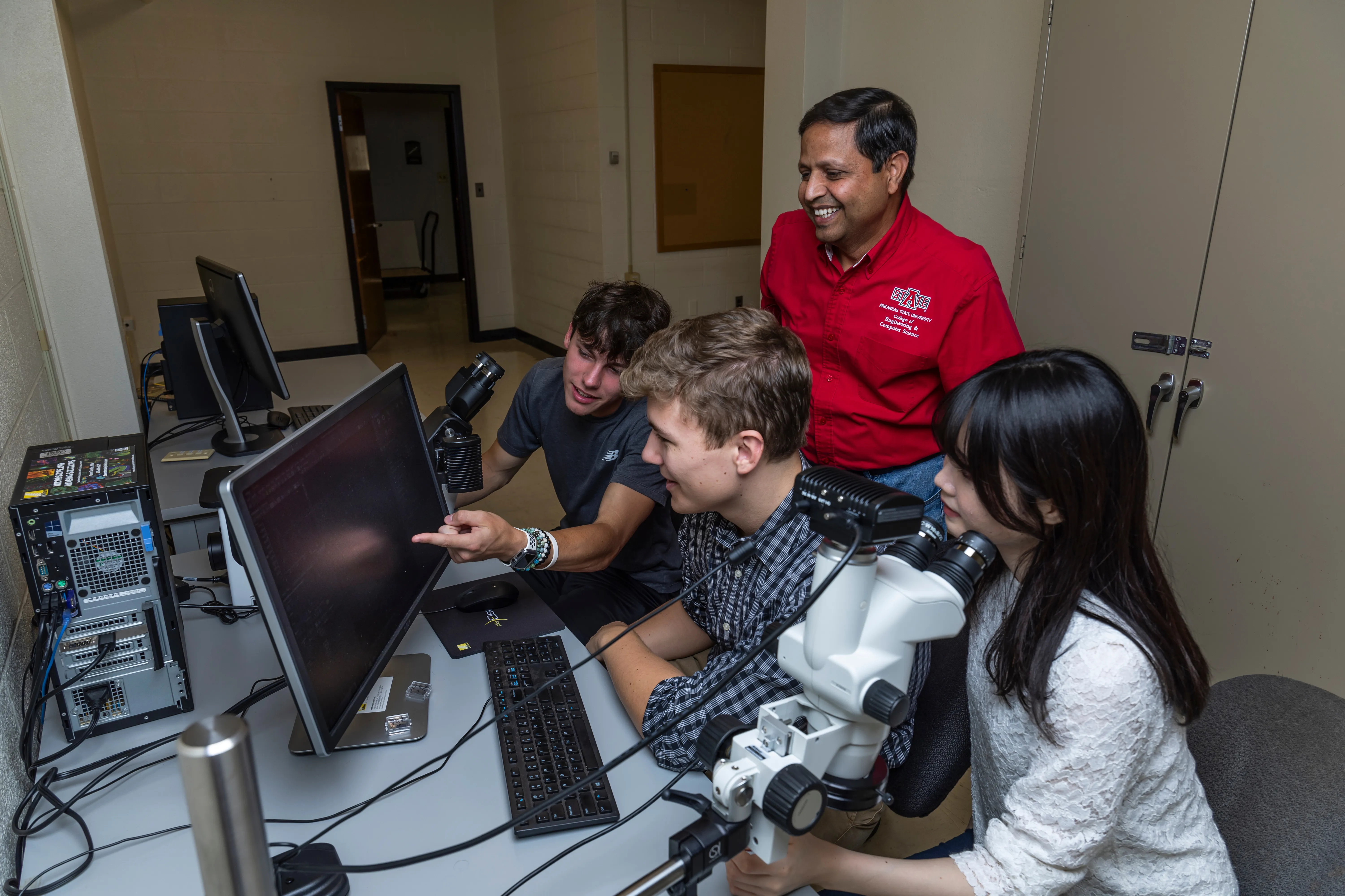 engineering technology students with dr. sharma going over labs with a microscope.