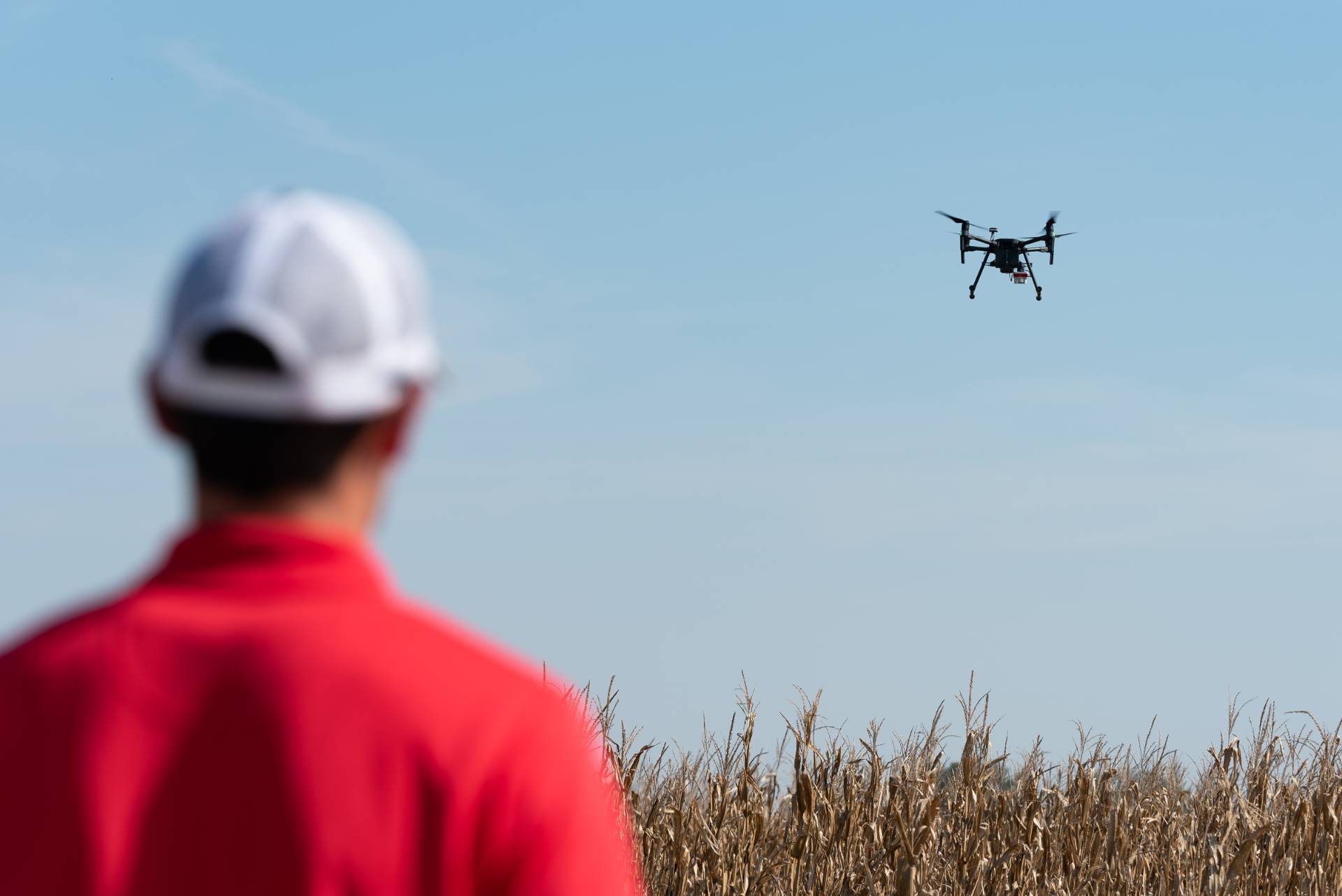 A student in the foreground controlling a drone as it flies over a field.
