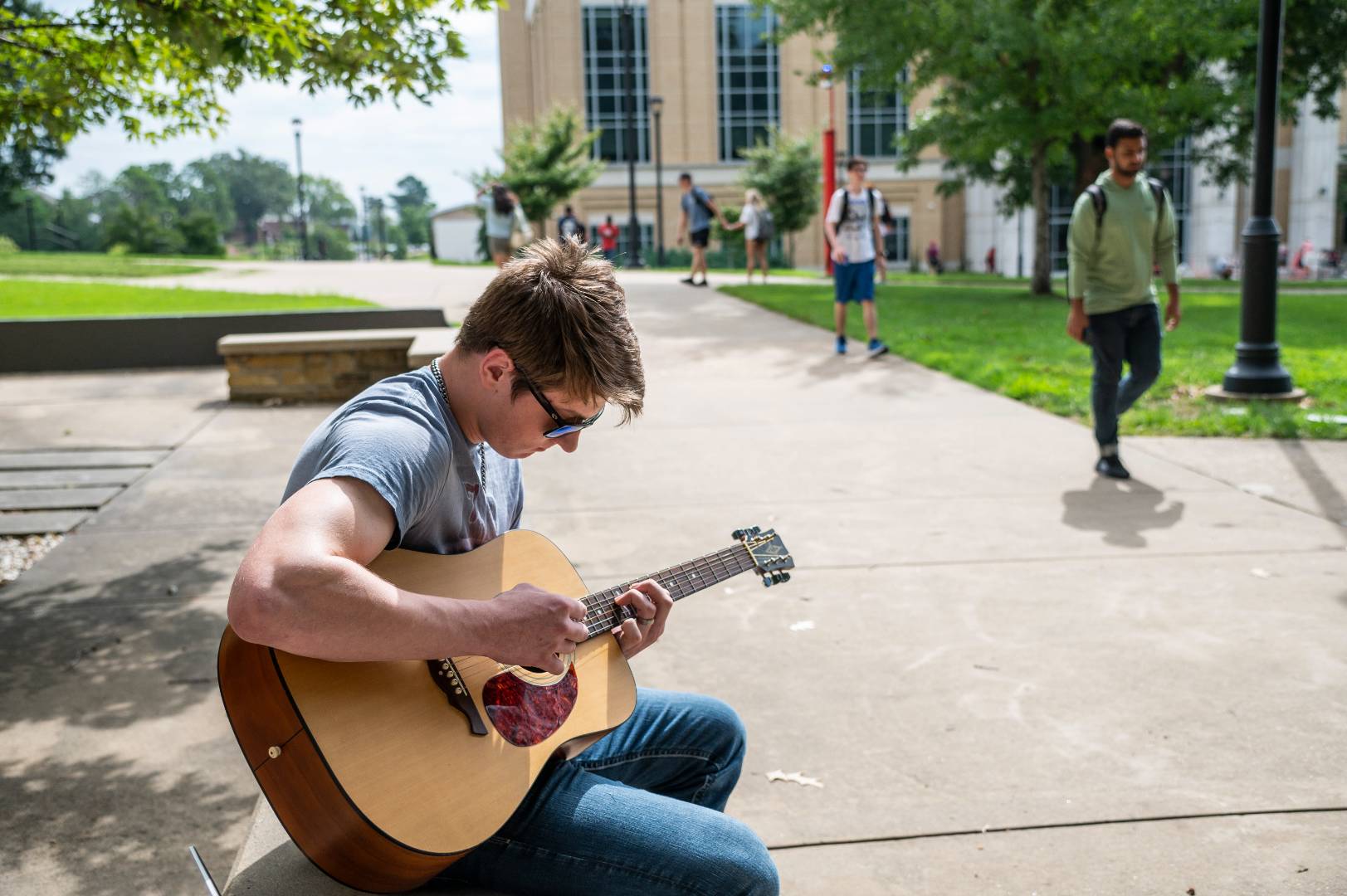 A student playing an acoustic guitar outside of the Humanities and Social Sciences building.