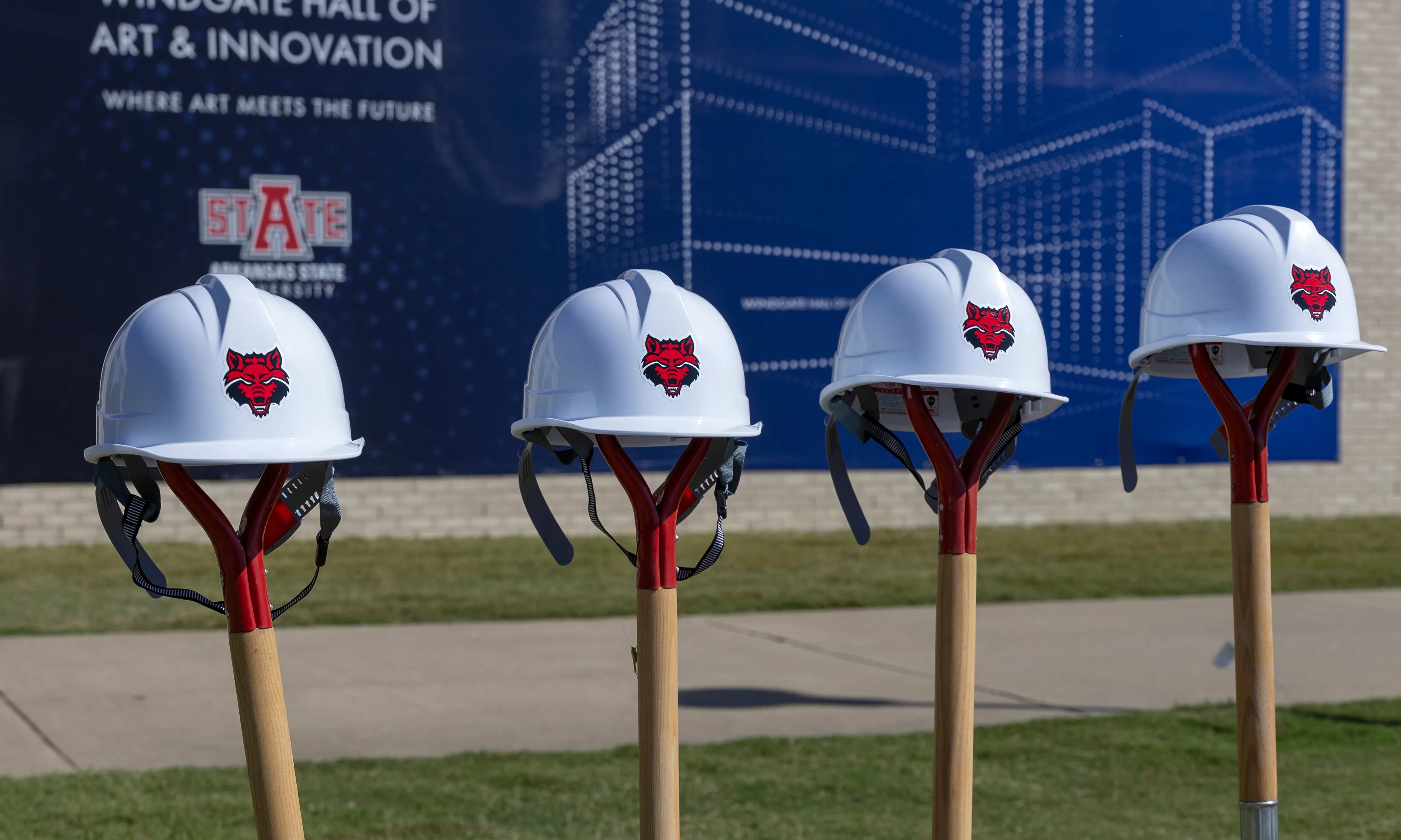  Building under construction with hard hats with redwolf logos on them sitting on top of shovels stuck in the ground.