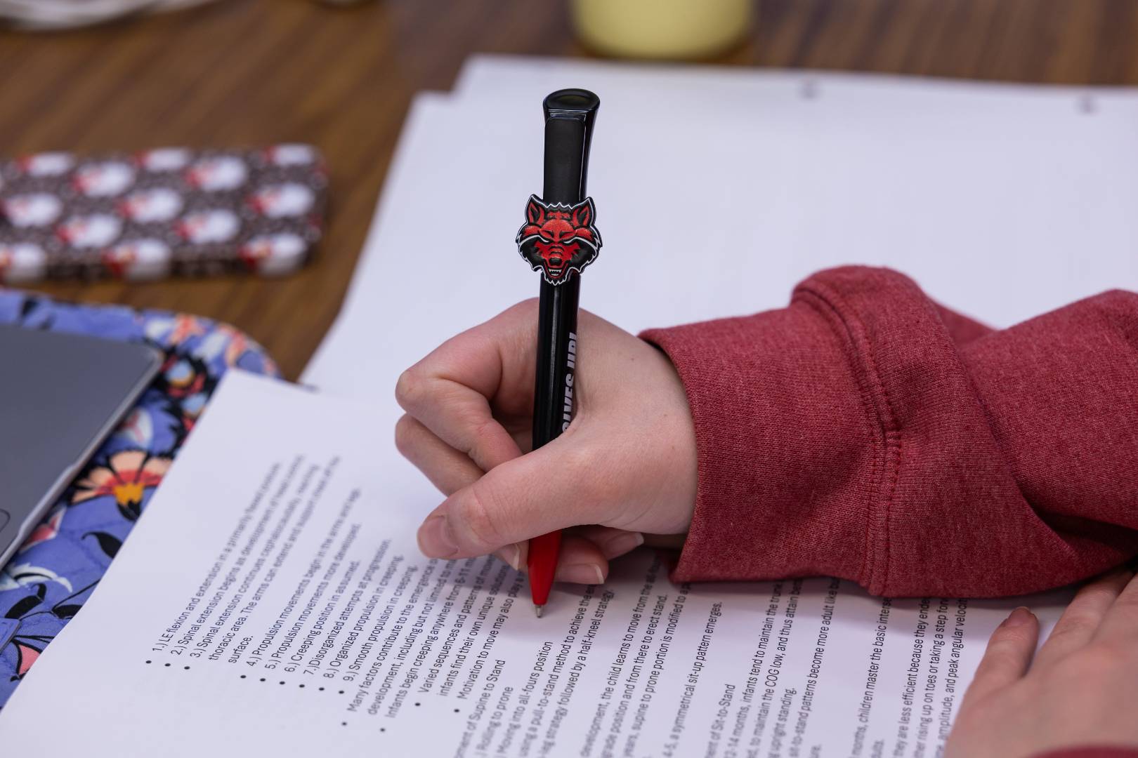 A close-up of someone writing with a pen that has a Red Wolf symbol.