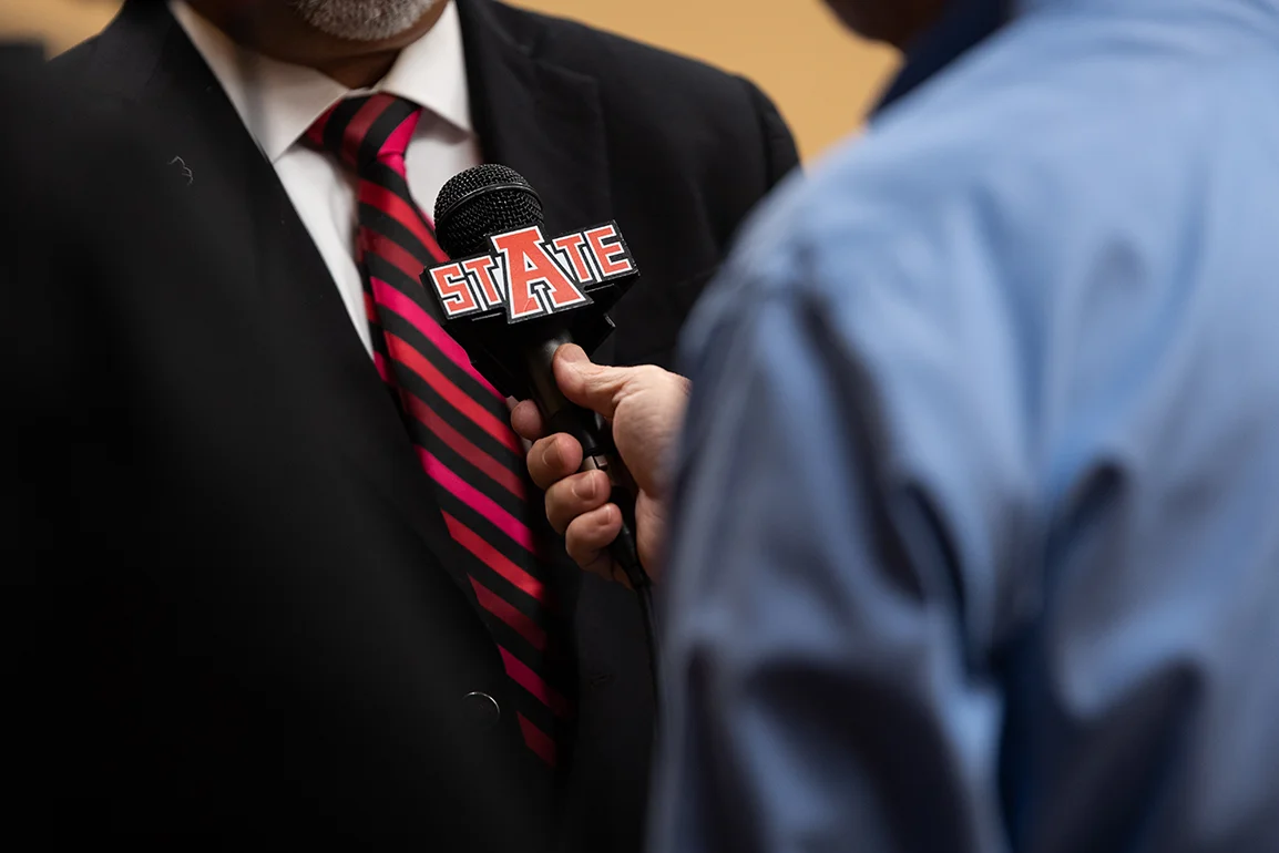 A close-up of someone holding a microphone with the A-State logo for an interview.