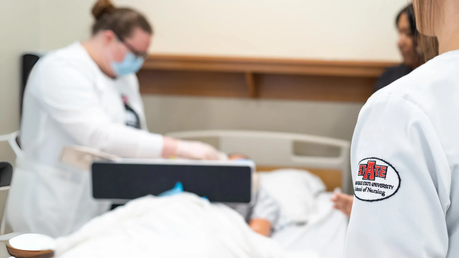 Nursing student blurred with lab coat on with A-State patch in focus.