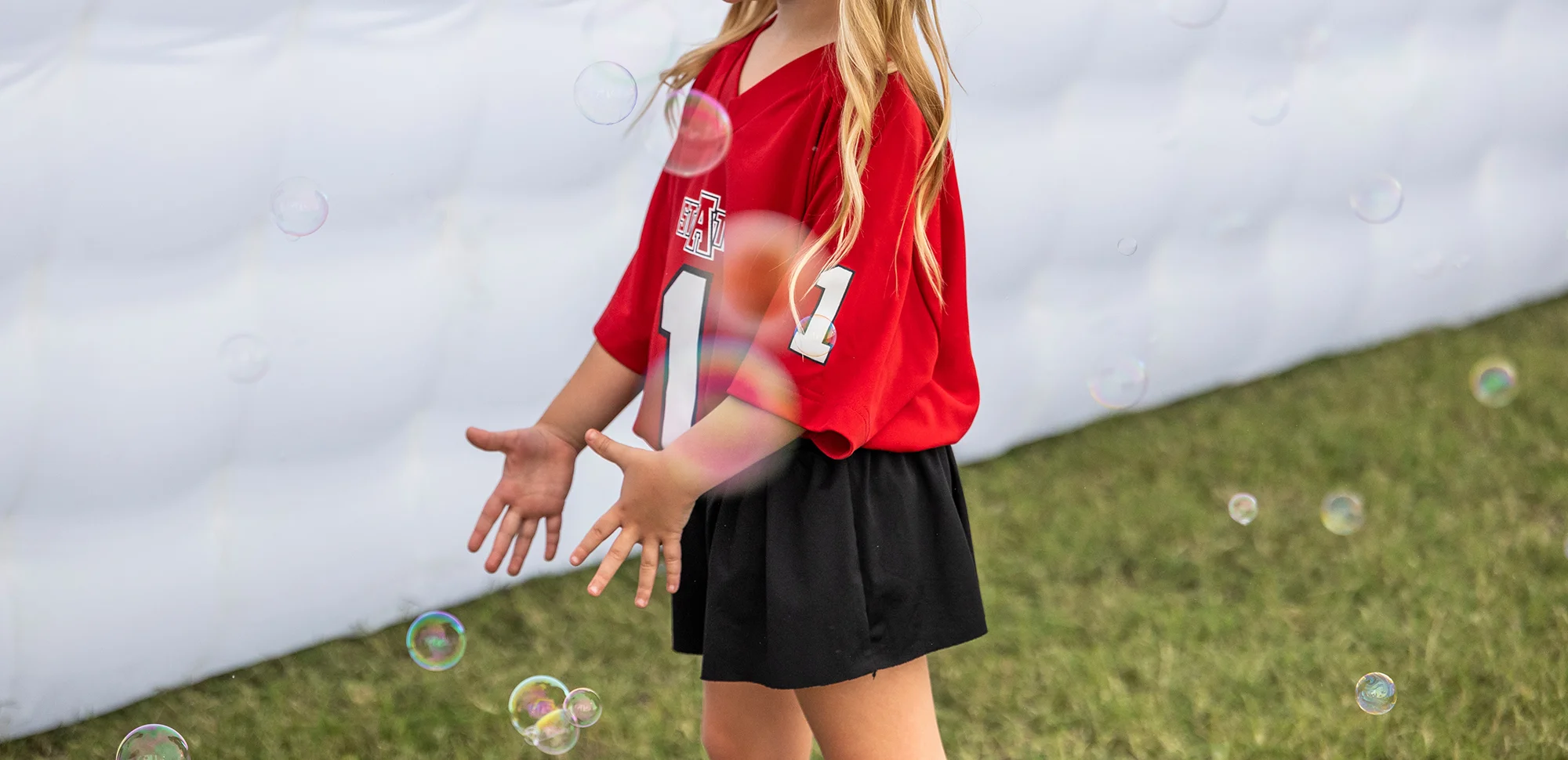 A neck-down photo of a child in A-State gear playing with bubbles