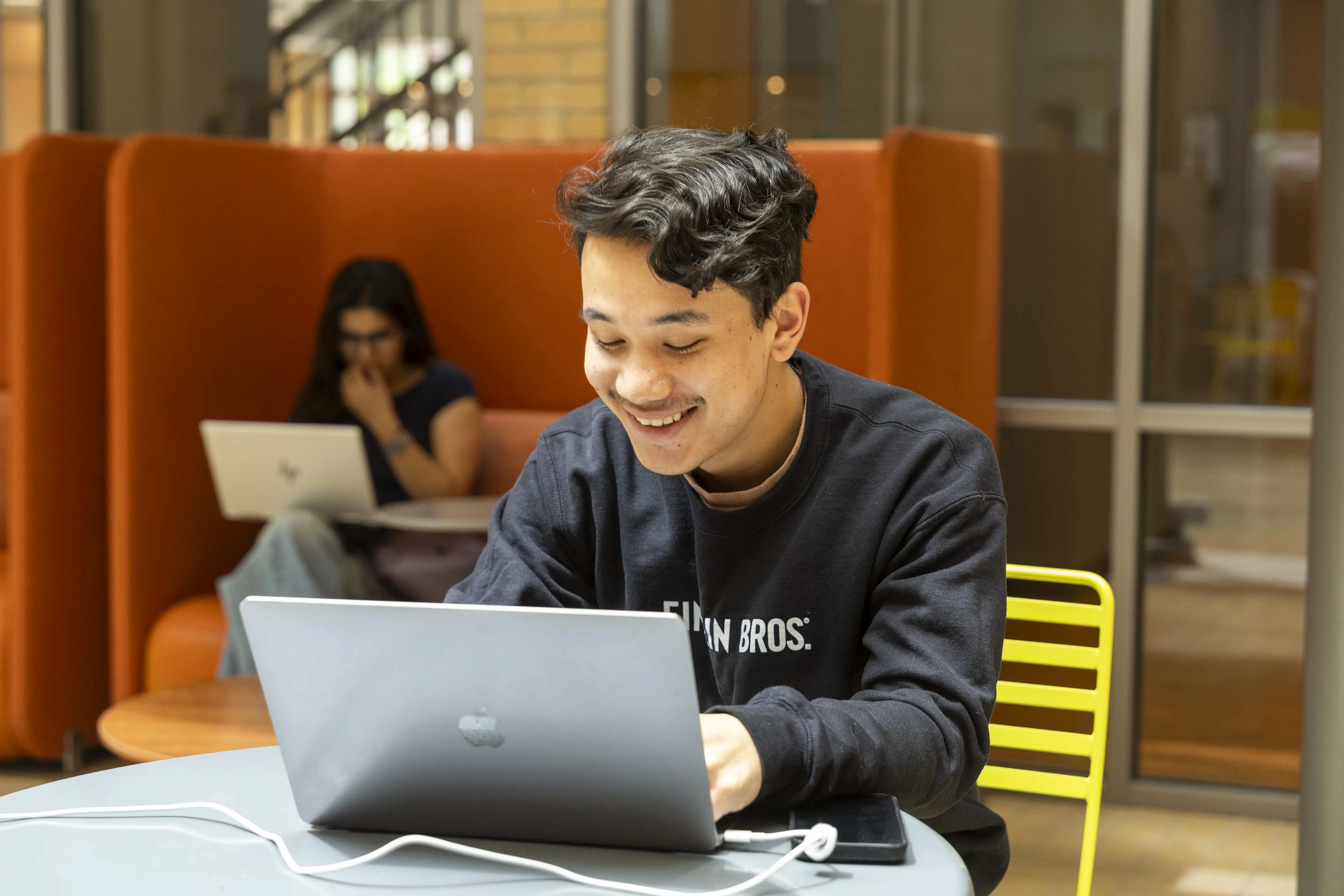 A student smiling as he works on his laptop.