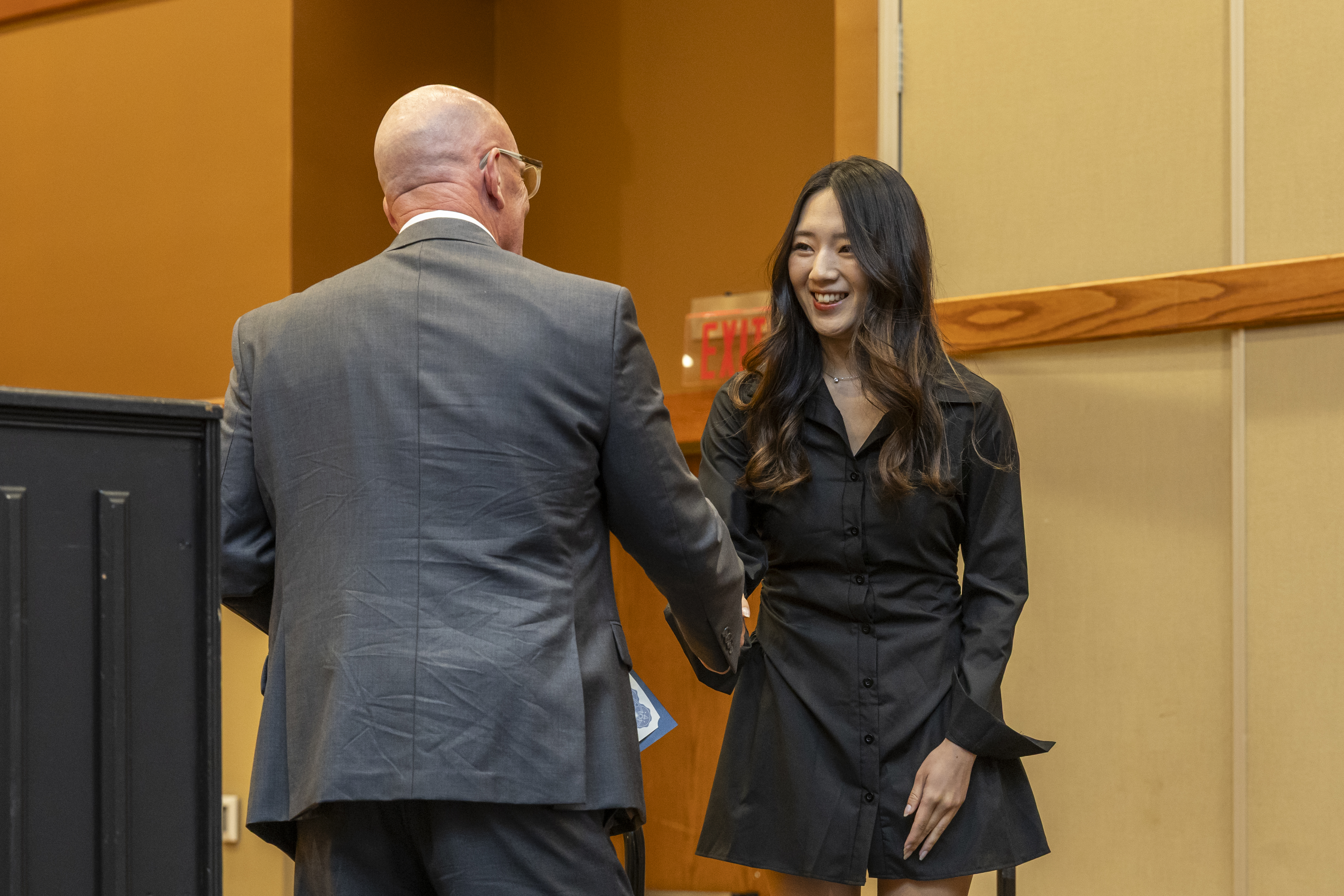 A student and professor shaking hands in formal attire.