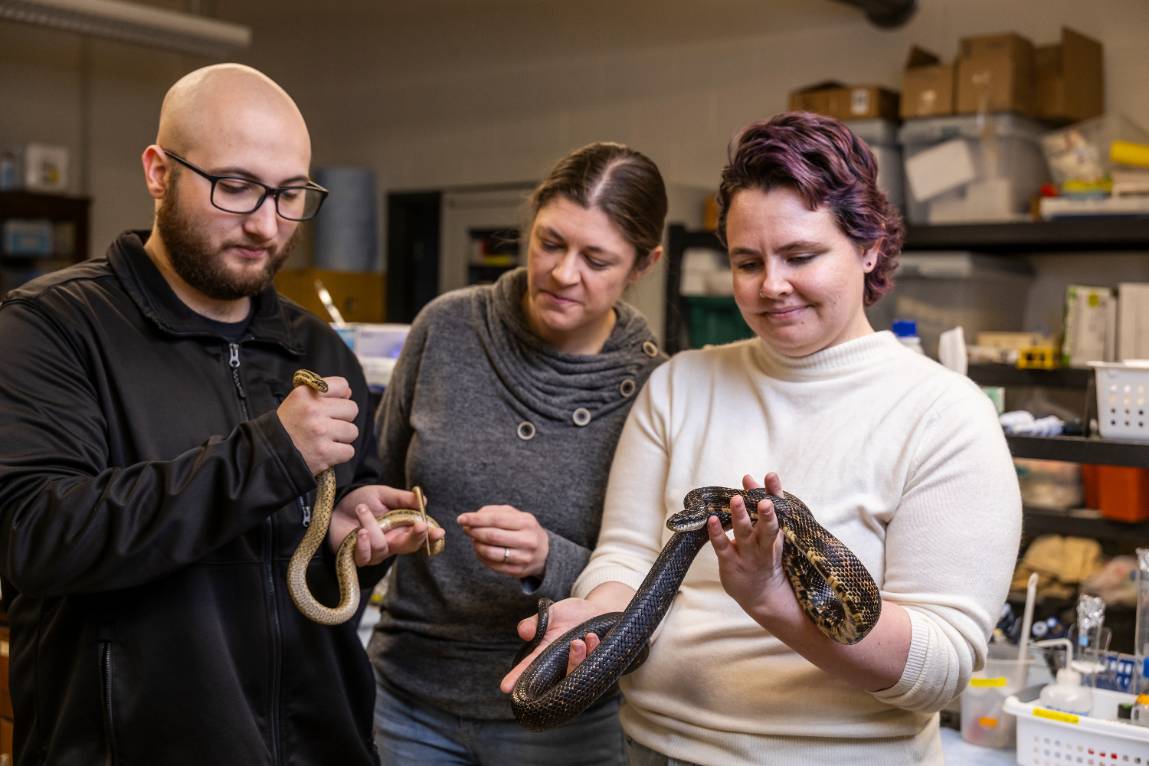A group of students and a professor holding snakes.