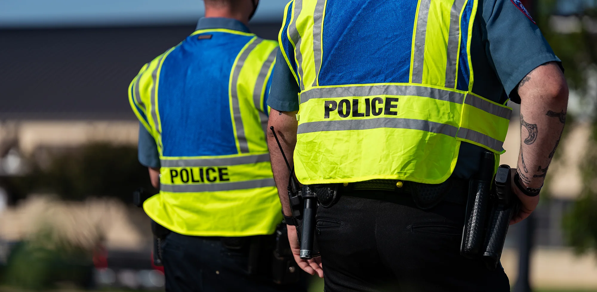 Two people wearing police visibility vests facing away from the viewer.