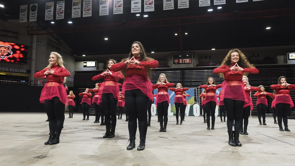 Group of performers in red outfits with sheer overlays standing in formation during a choreographed step show routine.