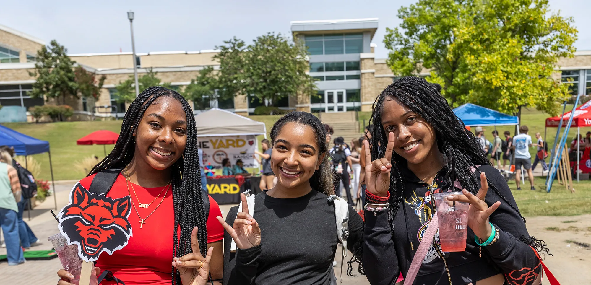 three smiling students at the community fair on a sunny day