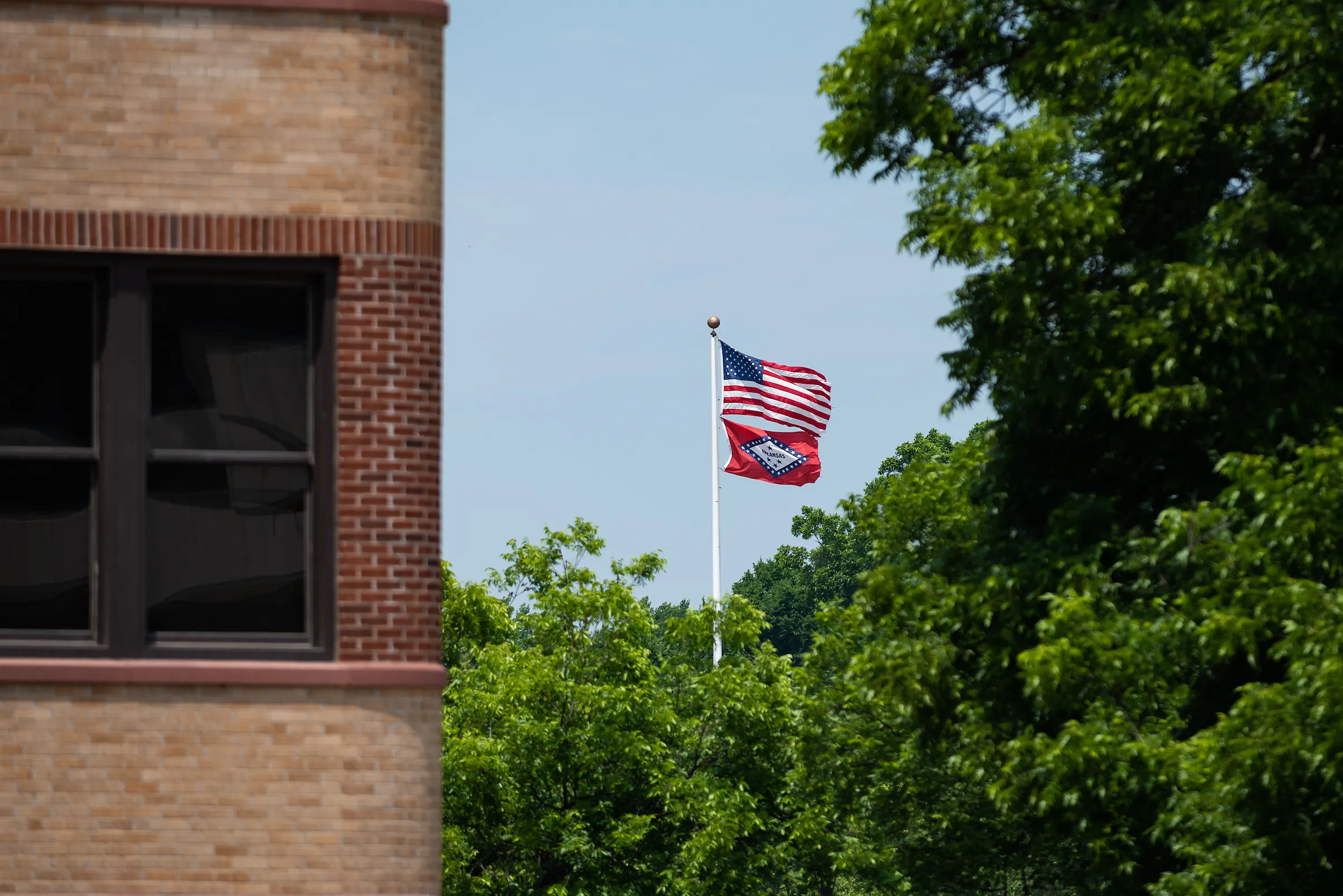 American and Arkansas flags wave above campus buildings surrounded by green trees.