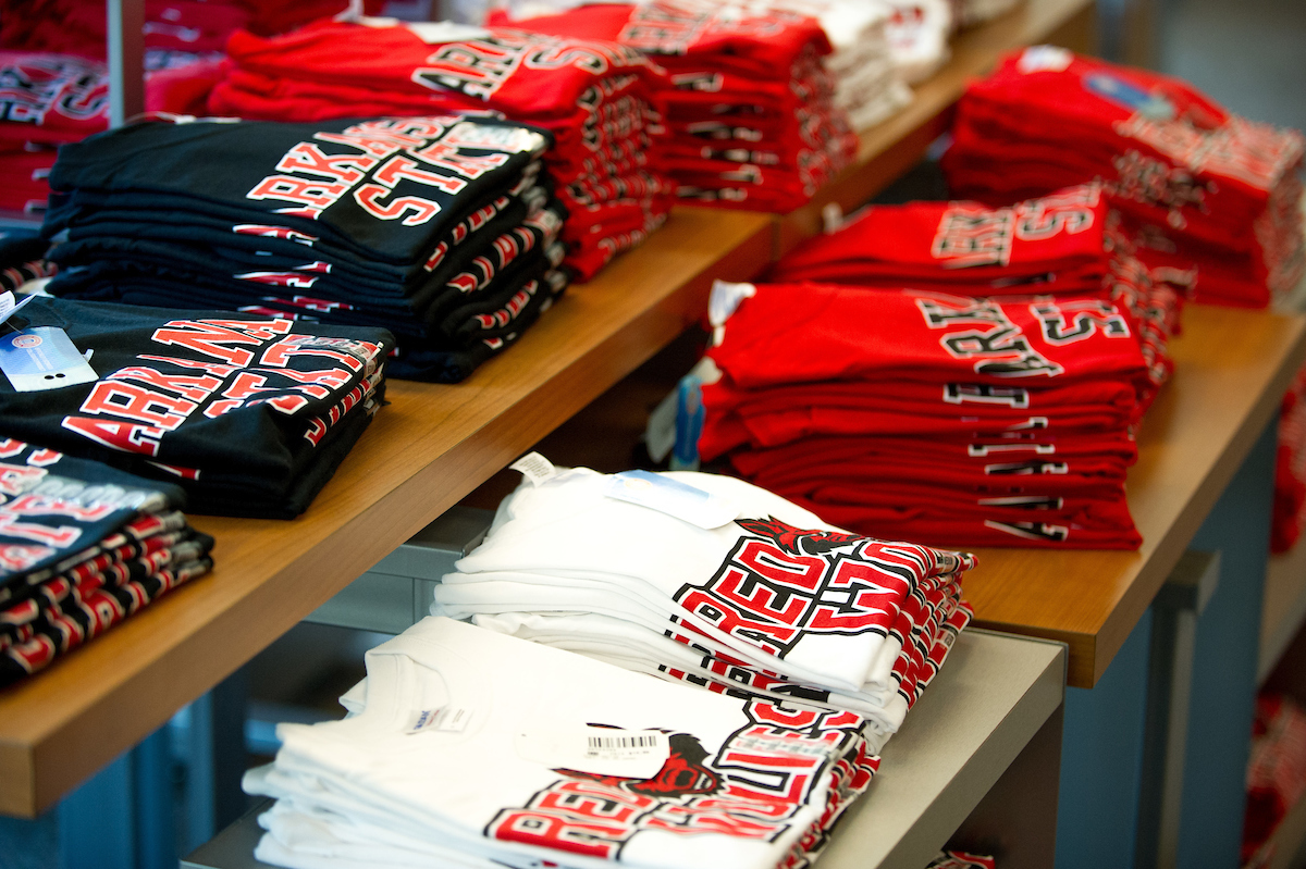 Folded Arkansas State University T-shirts in black, red, and white on display in a campus store.