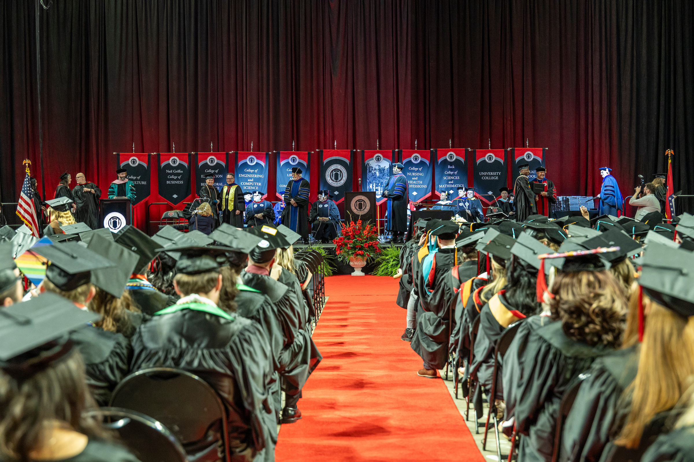 Graduates seated at a commencement ceremony with faculty on stage.