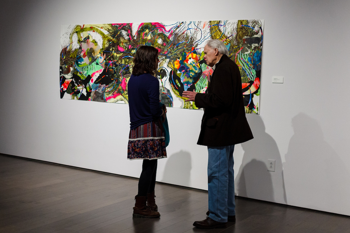 Two people talk in front of an artwork exhibit at the Bradbury Art Museum