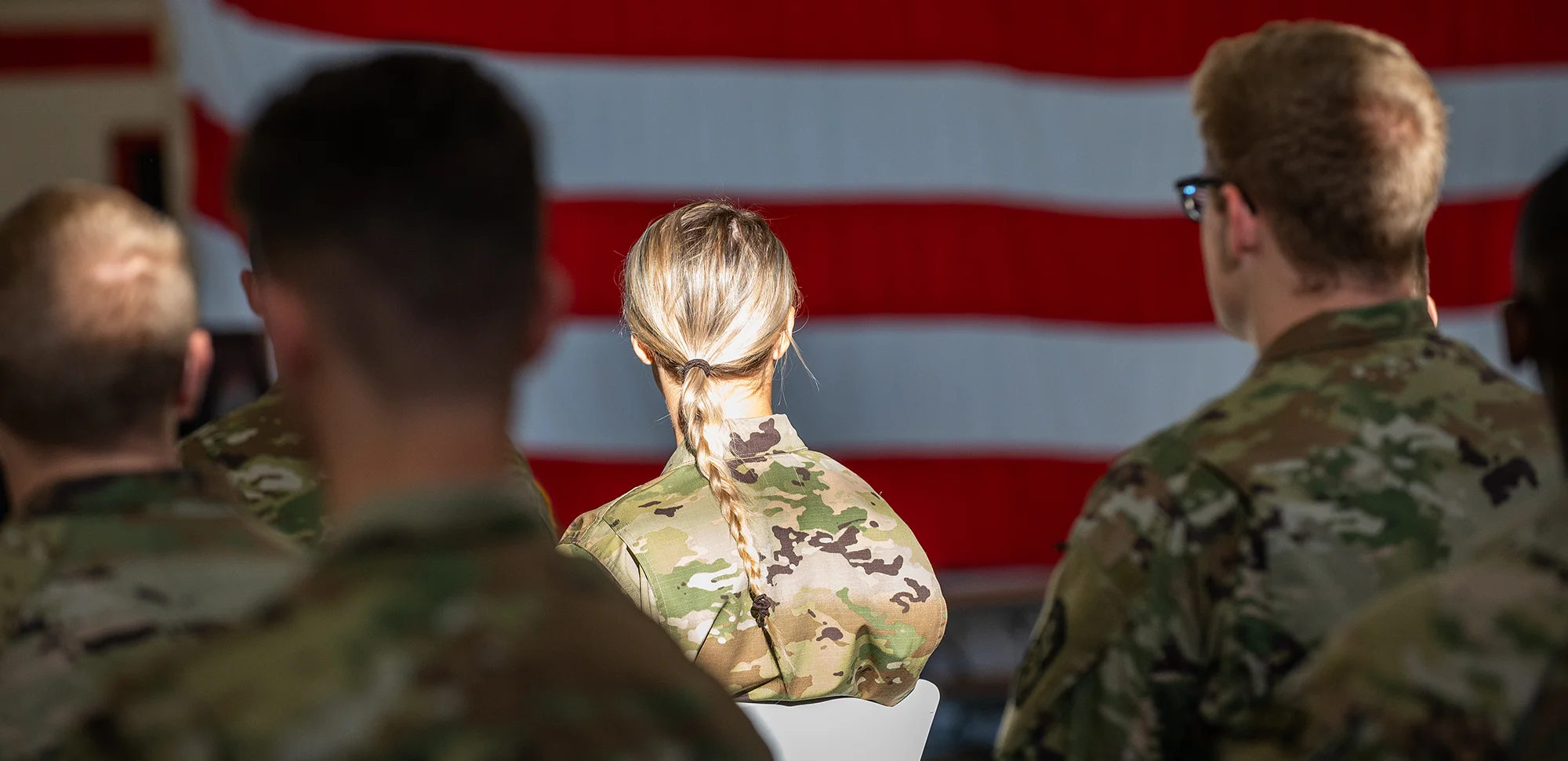 A-State cadets sitting in front of the American flag, looking away from the camera.