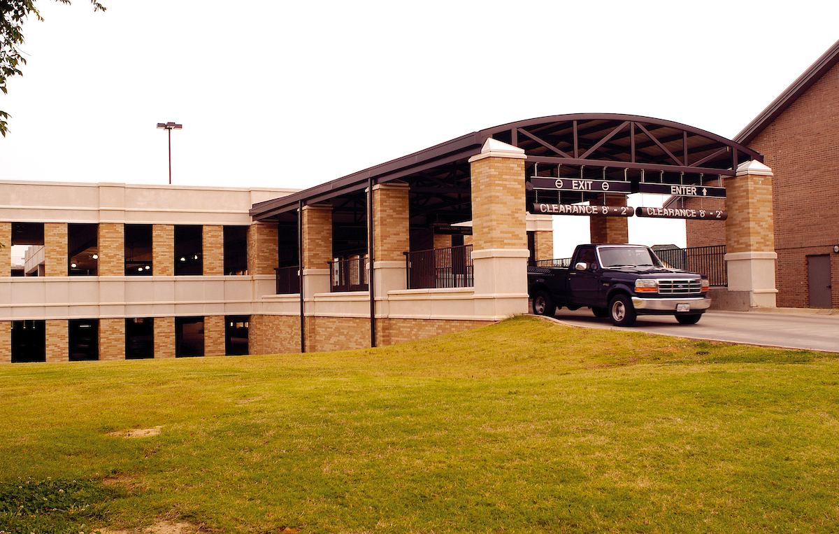 AState parking garage entrance with a clearance sign and a black pickup truck driving up the ramp on a partly cloudy day.