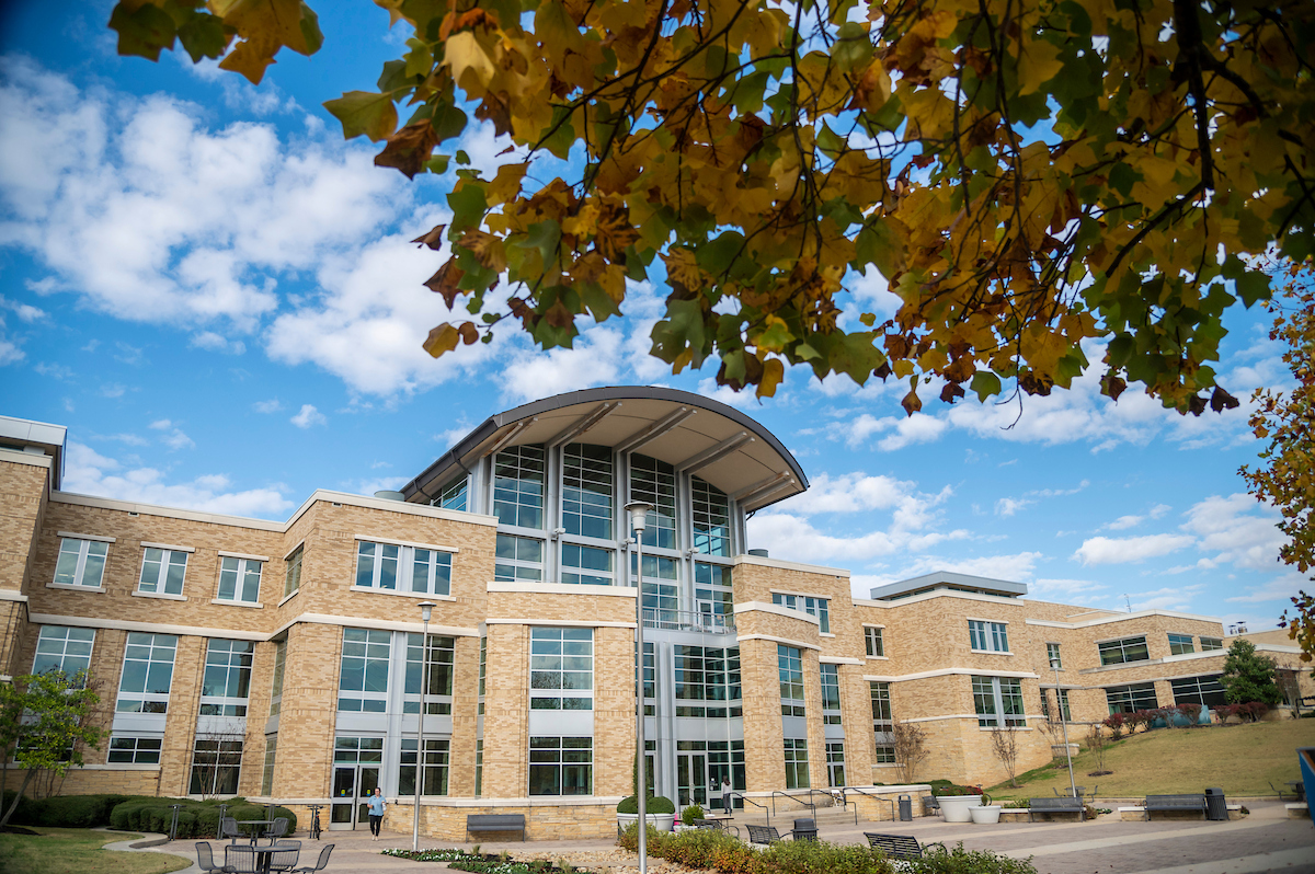 A-State Student Union framed by fall leaves under a bright blue sky with scattered clouds.