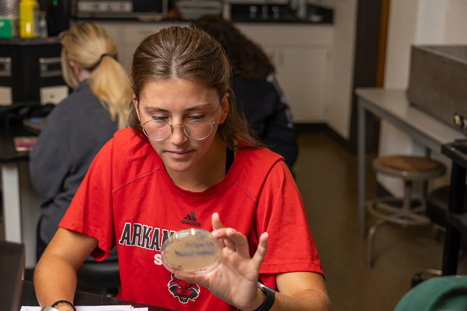 A student in a Red Wolves shirt inspecting a petri dish.