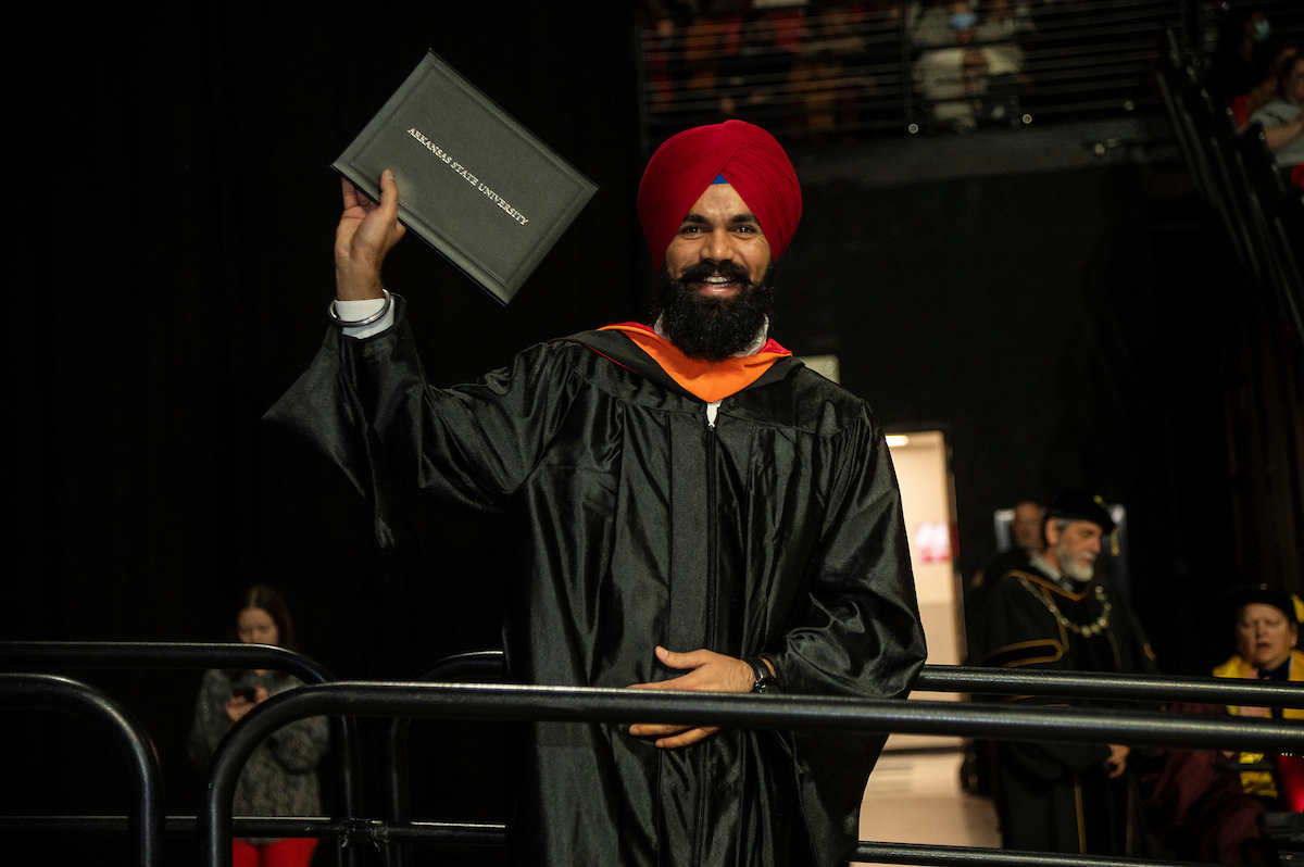 A joyful A-State graduate proudly holds up diploma during a commencement ceremony.