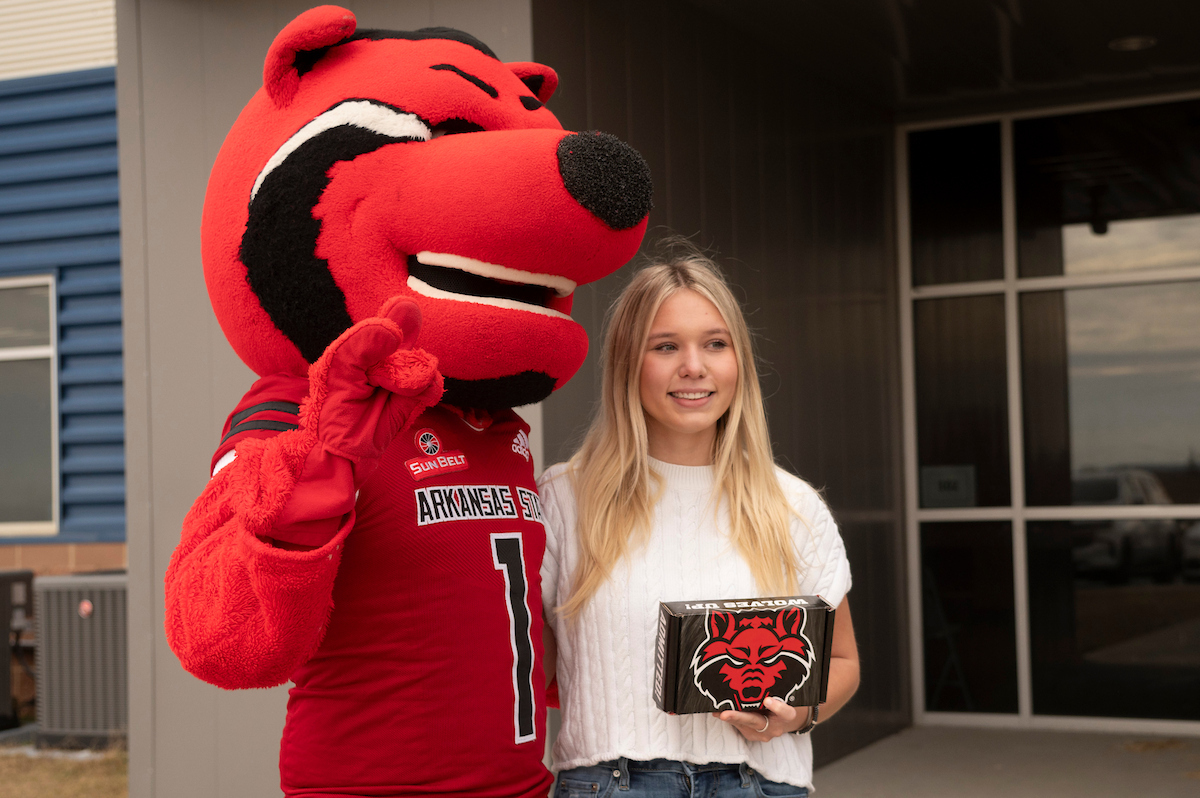 A student poses with Howl, the A-State mascot, while holding a scholarship presentation box.