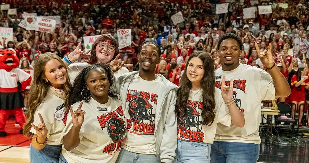 Student Activities Board students with their hands making a 'wolves up' sign in front of a crowd of students at the Order of the Pack pep rally.