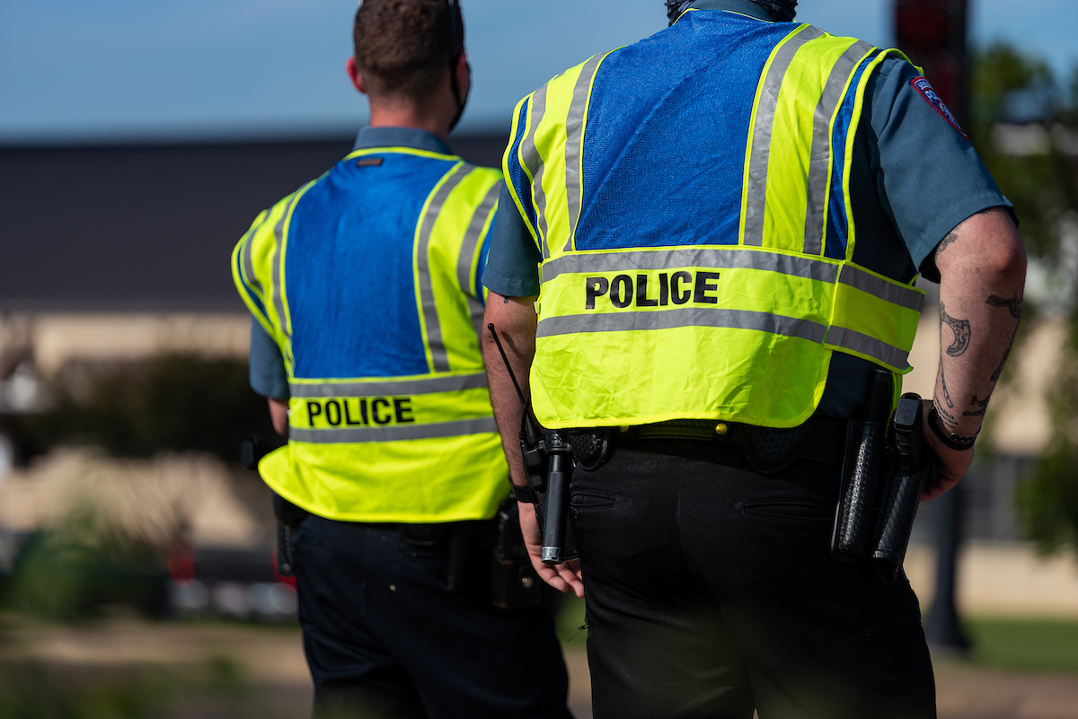 Campus police officers are seen from behind, looking out onto campus.