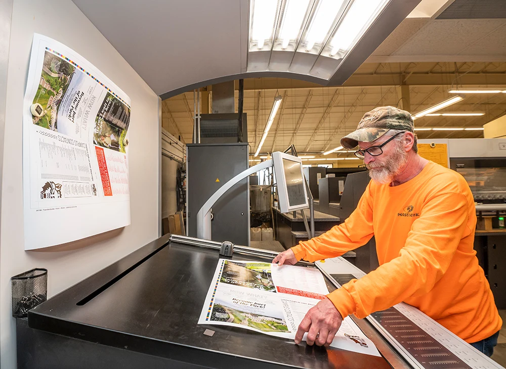 A Printing Services worker using a machine to cut down a print.