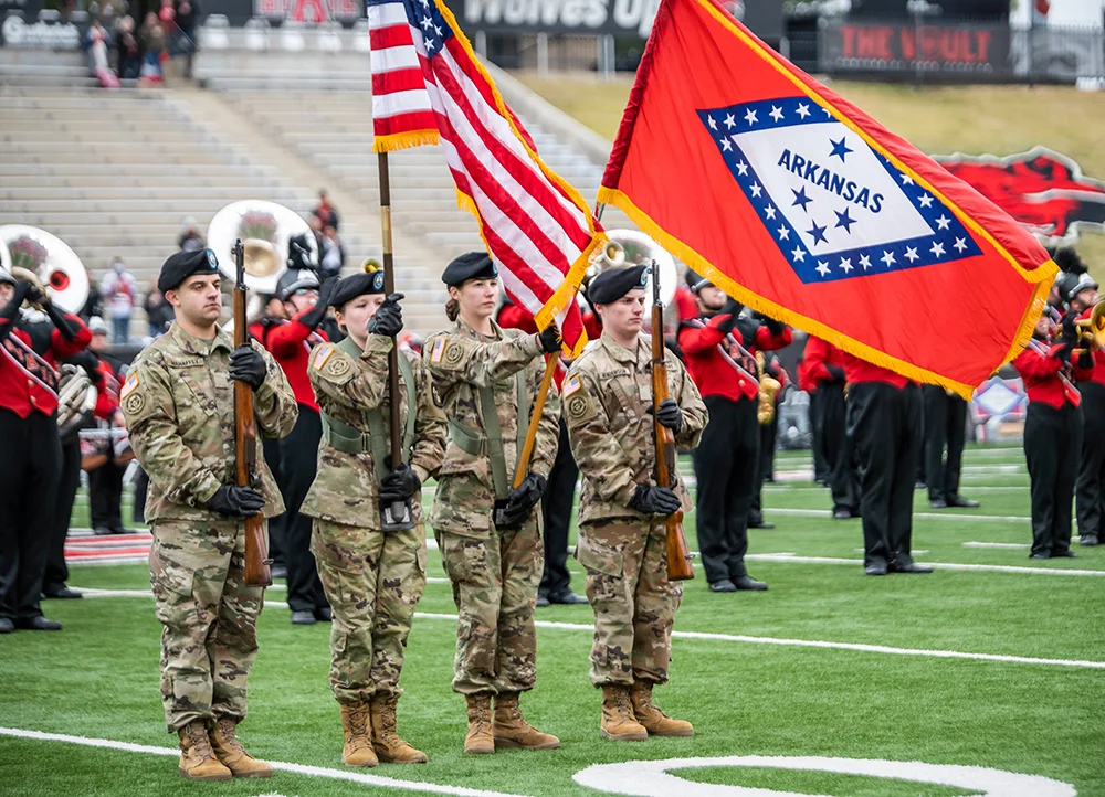 A-State ROTC cadets holding flags and rifles at a football game.